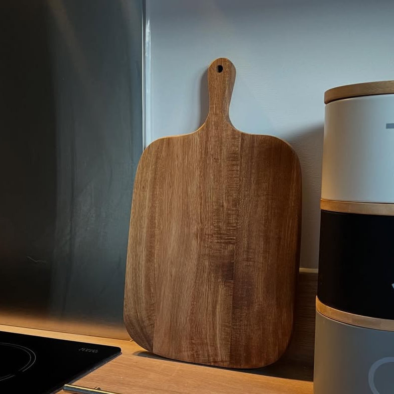 Wooden cutting board leaning against a wall next to a kitchen appliance.