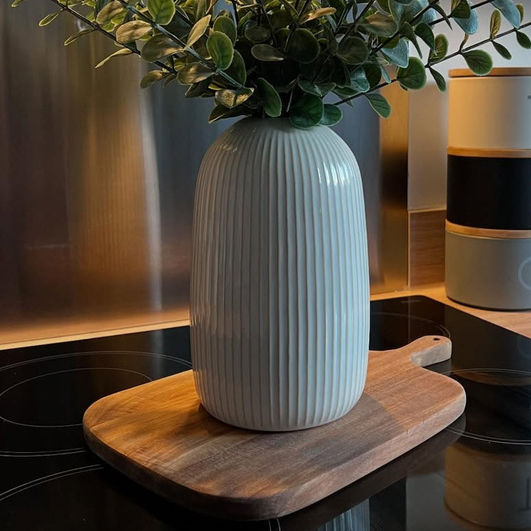 White vase with green plant, styled on a acacia wooden chopping board in a kitchen setting