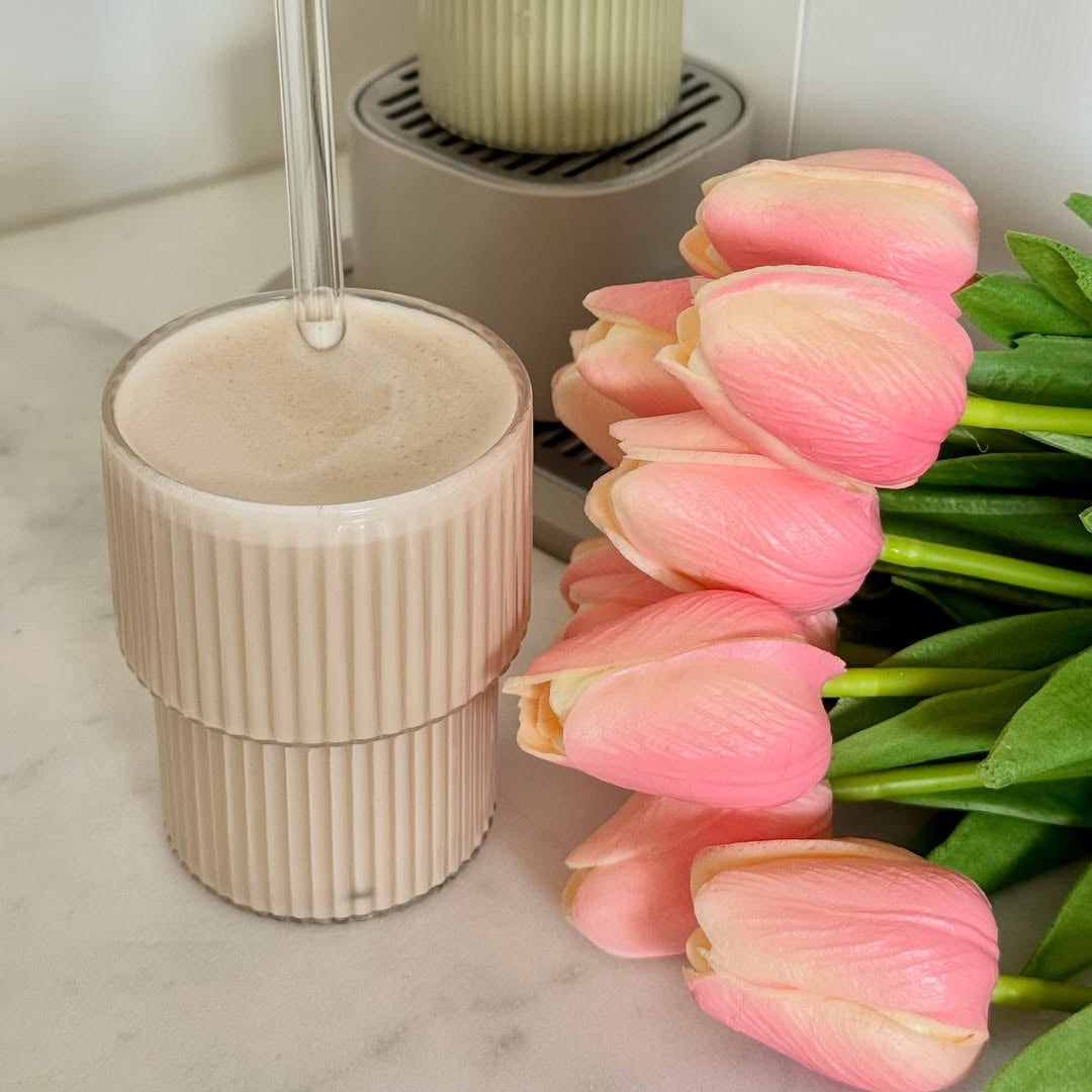 Cup of coffee with a straw next to pink tulips on a marble surface