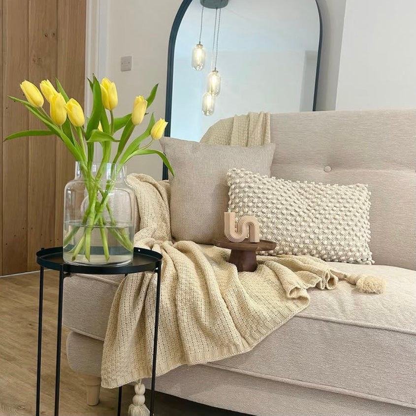 Living room with a beige sofa, decorative pillows, and a vase of yellow tulips on a side table.