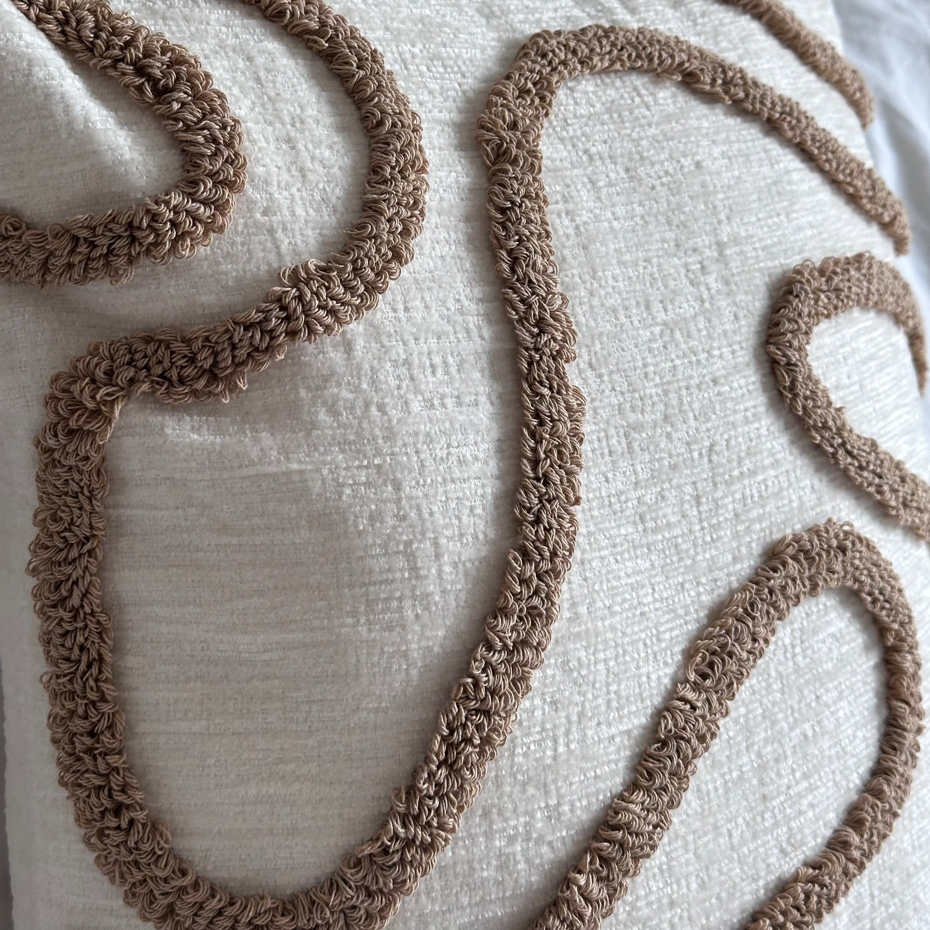 Decorative pillow with brown embroidered patterns on a wooden surface