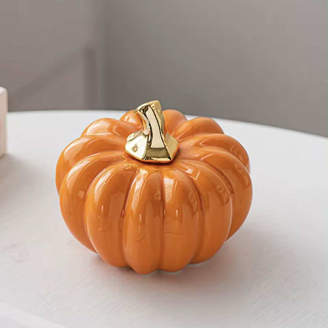 Decorative orange pumpkin with a gold stem on a white surface