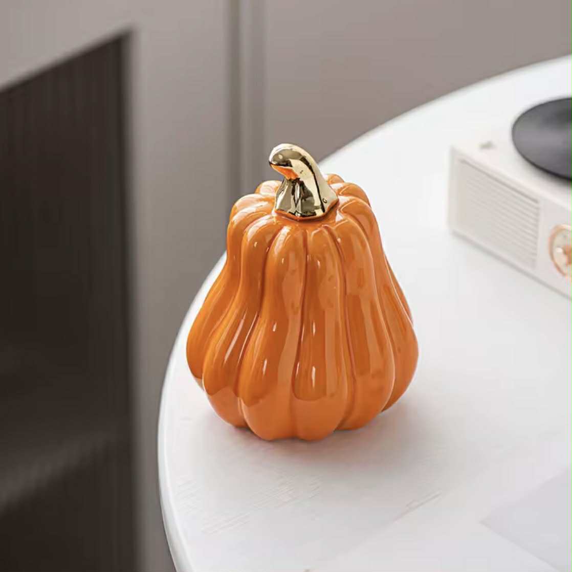 Decorative orange pumpkin with a gold stem on a white surface.