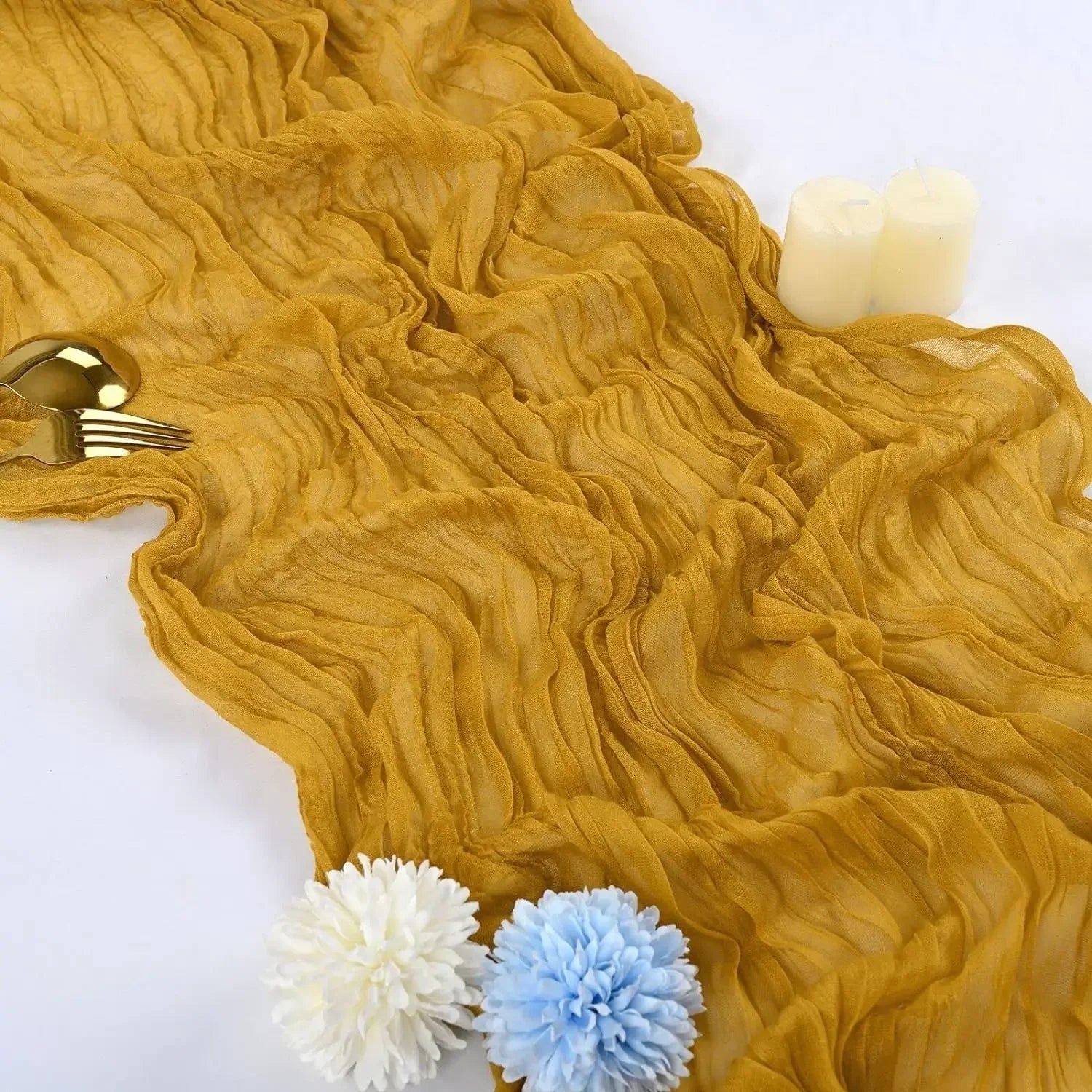 A close-up of a mustard cheesecloth rustic table runner draped on a white surface.