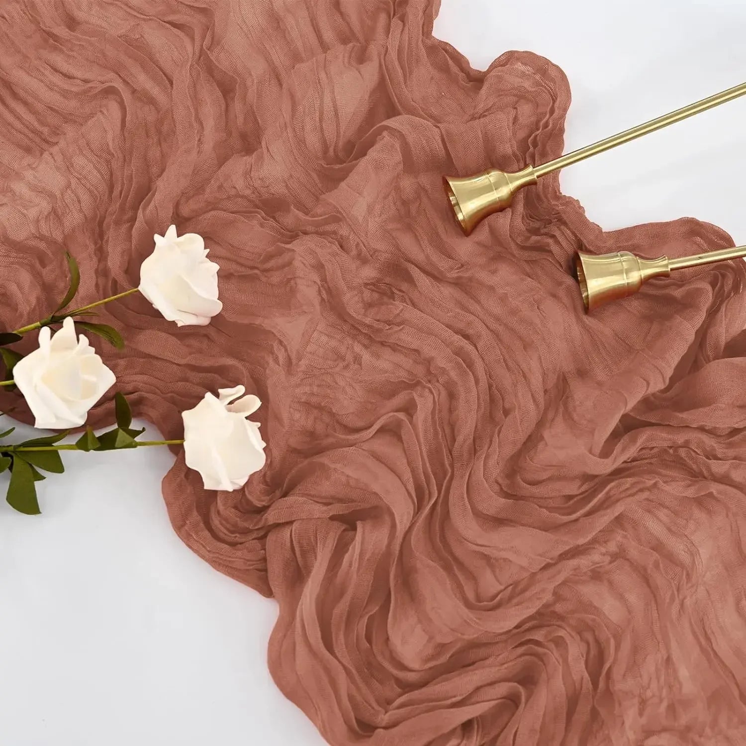 A close-up of a pink cheesecloth rustic table runner draped on a white surface, with three flowers placed nearby.