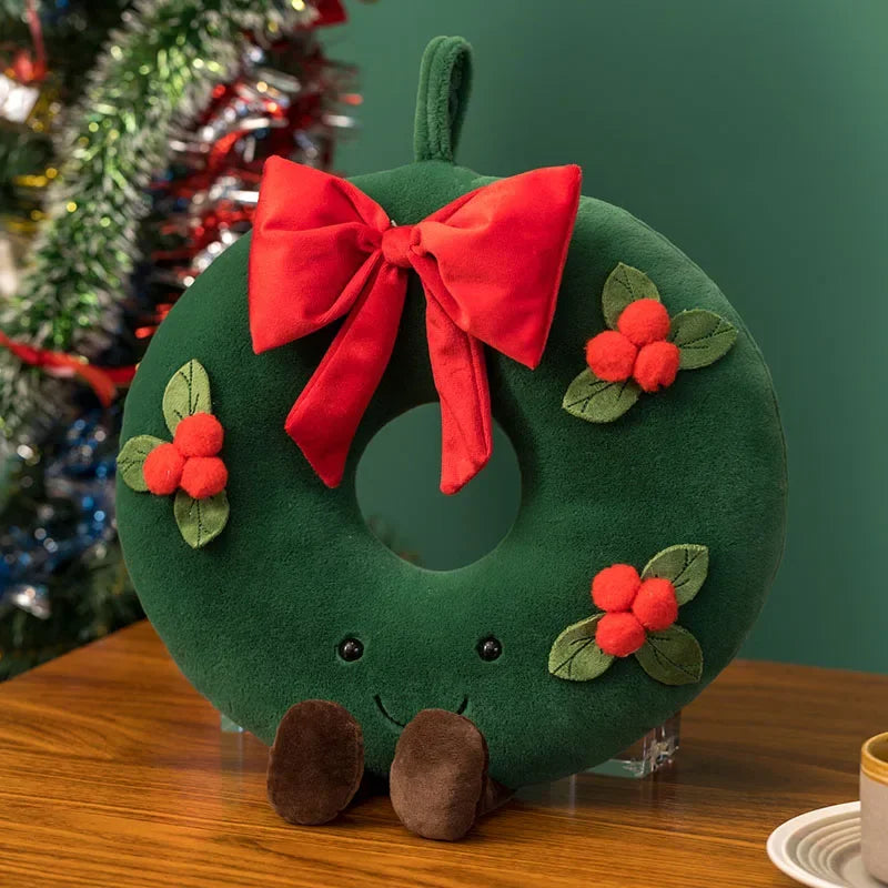 A soft sculptural Christmas plush pillows, shown in the styles of a wreath that has a smiling face and feet.