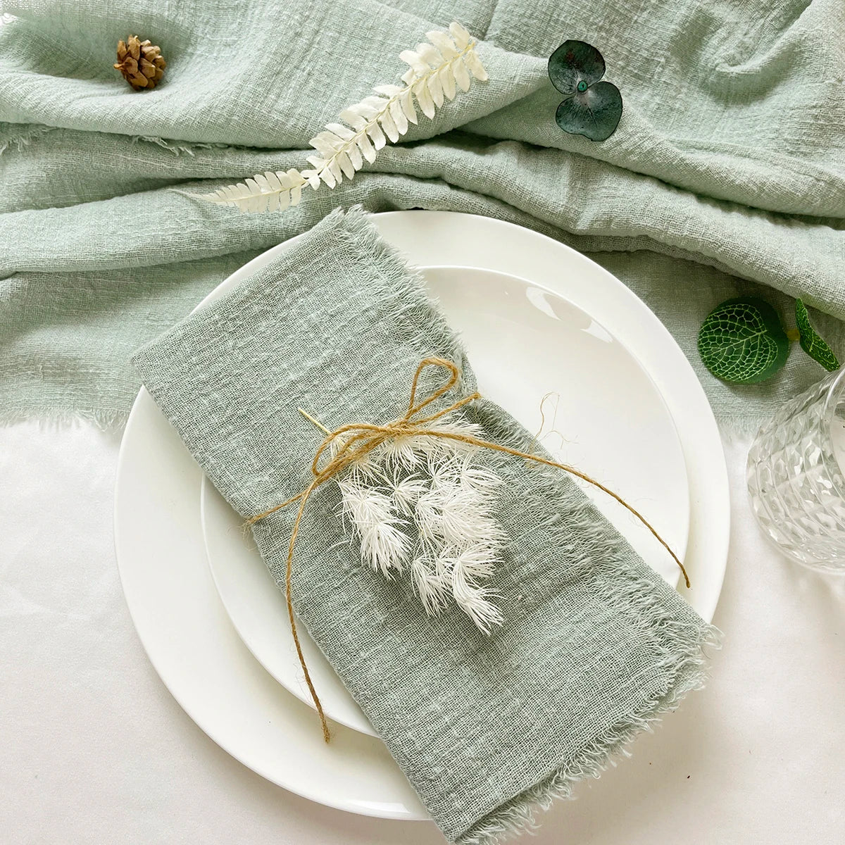 A light green cotton napkin is draped over a white ceramic plate, with a decorative tassel-like string attached to the napkin.