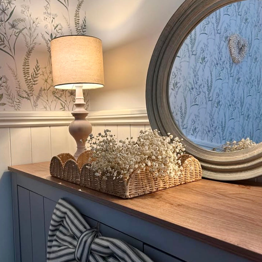 Decorative setup with a lamp, basket of dried gypsophila flowers, and mirror on a wooden surface.