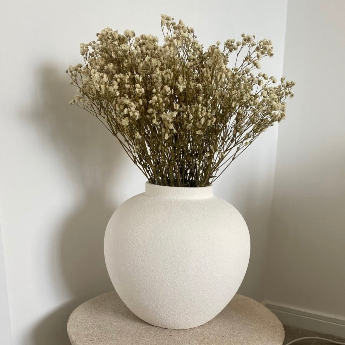 White vase with dried gypsophila flowers against a plain wall