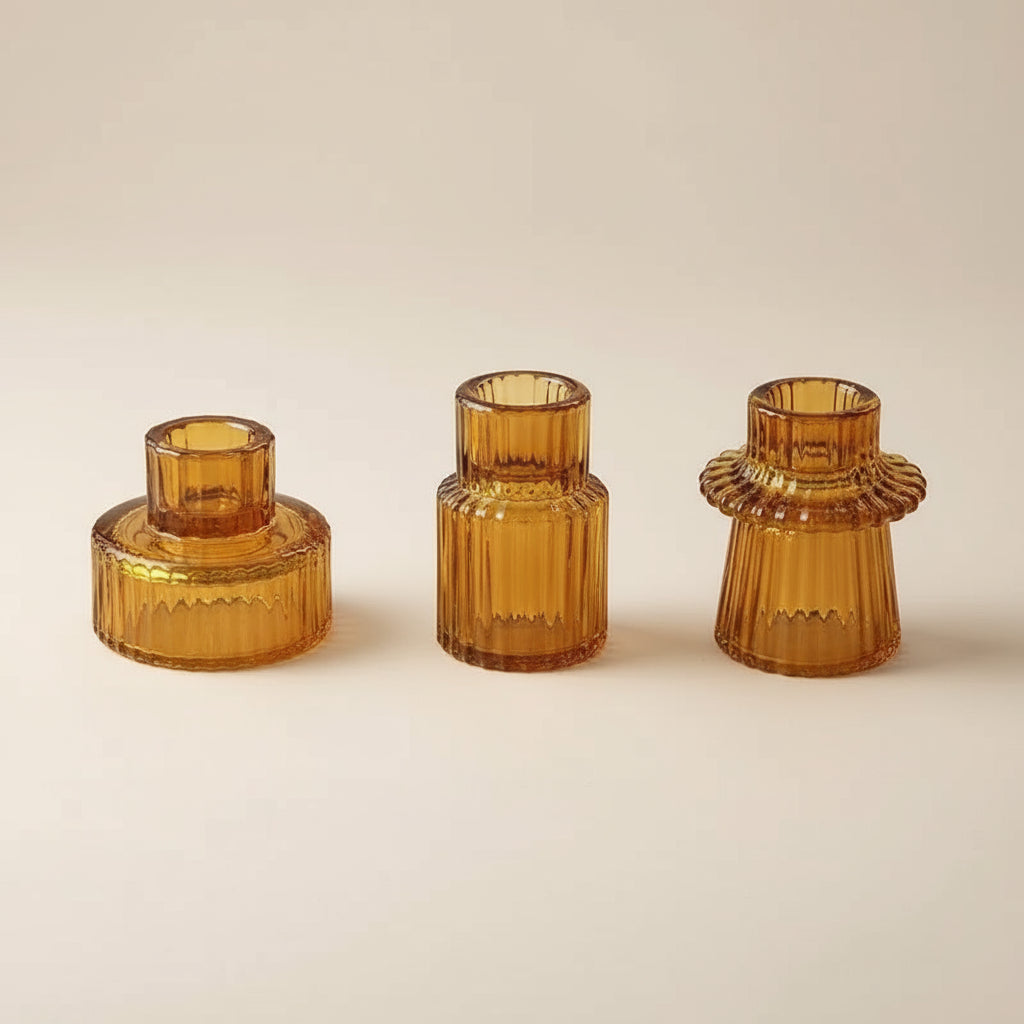 Three glass candlestick holders on a white surface. The holders have a textured, geometric, design in an amber colour.