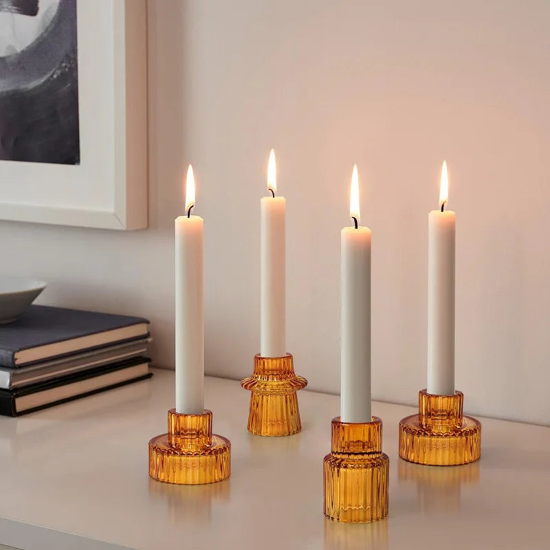 Three glass candlestick holders on a white surface, with each holder holding a lit candle. The holders have a textured, geometric, design in an orange-brown color.