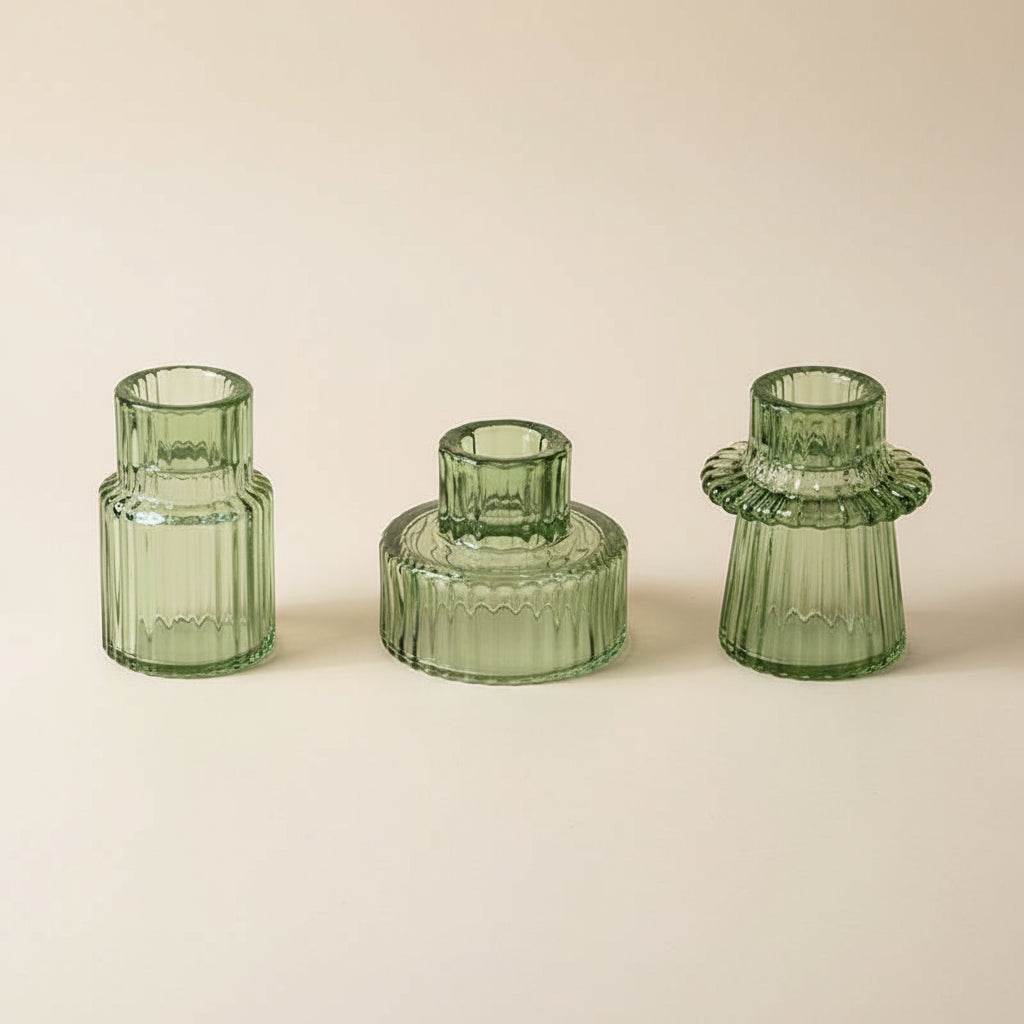 Three glass candlestick holders on a white surface. The holders have a textured, geometric, design in an green colour.