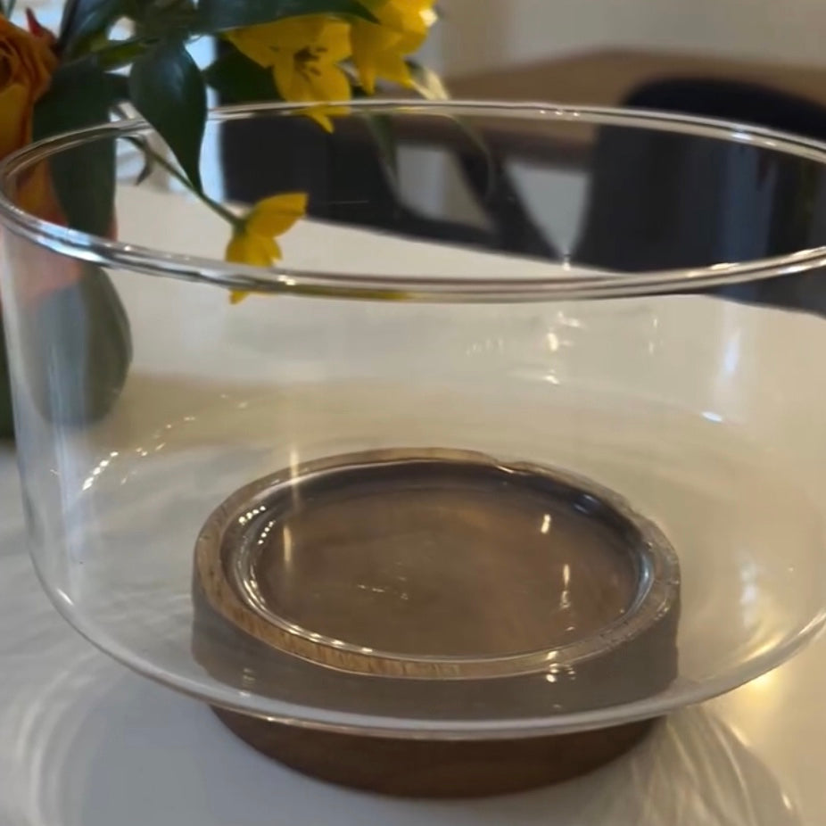 Clear, empty glass bowl with a wooden base on a white surface