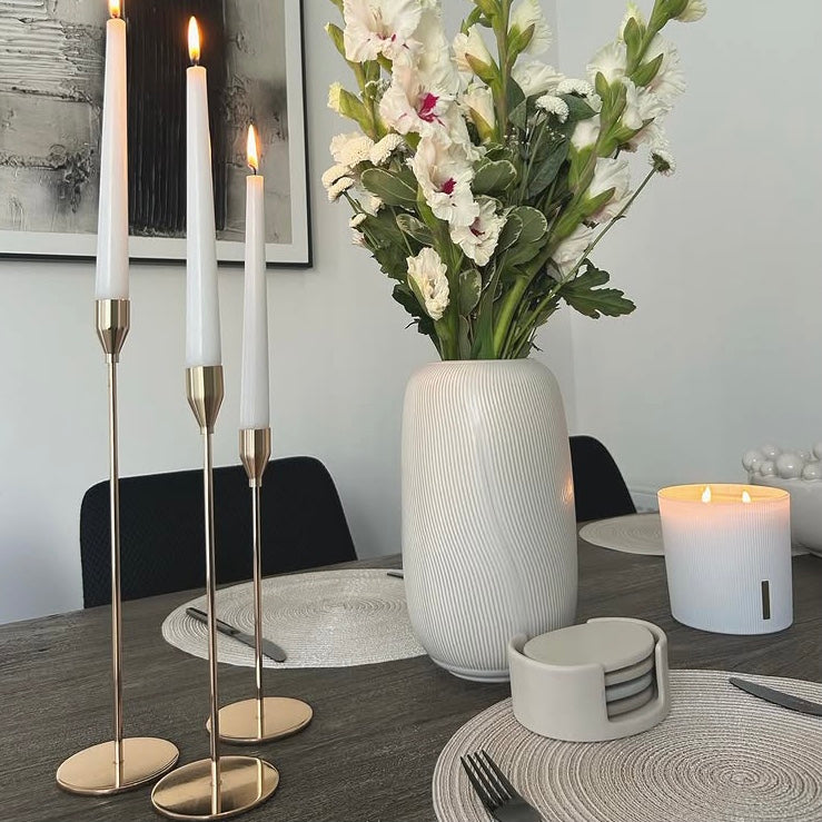 Dining table setting with three gold finish candle holders, a vase of flowers, and place settings.