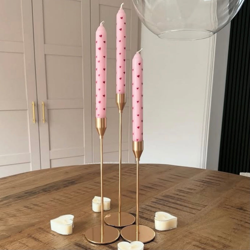 Three pink candles with gold holders on a wooden table