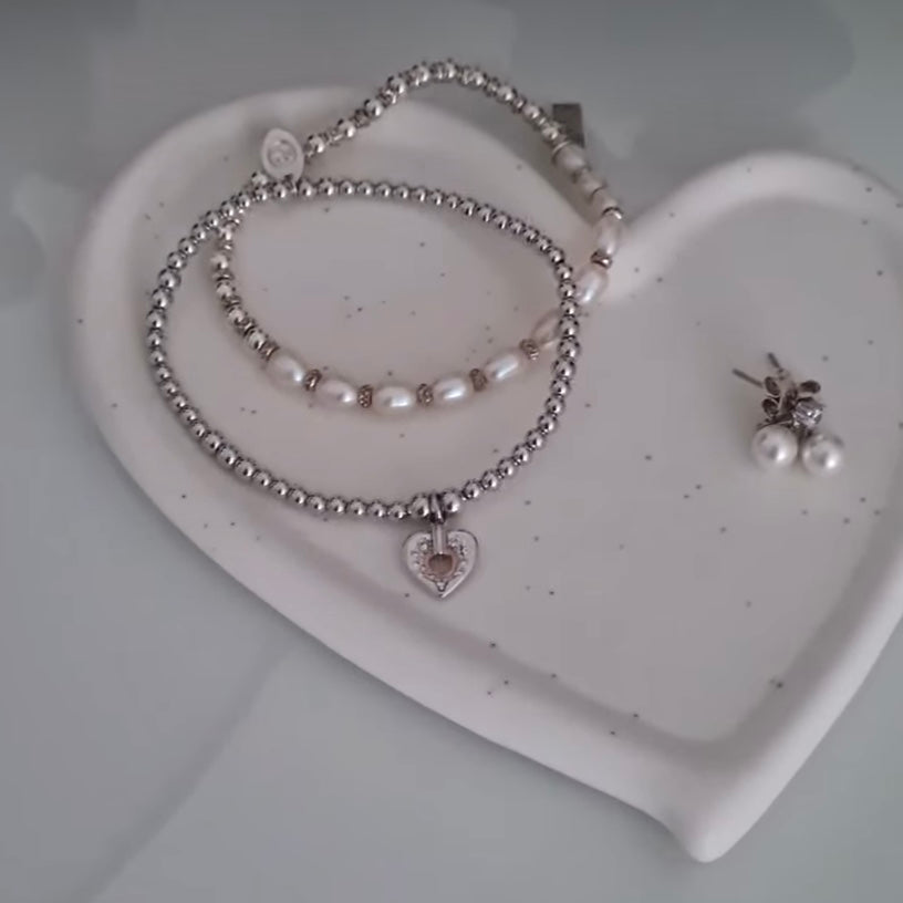Jewelry set with a bracelet and earrings on a heart-shaped white dish.