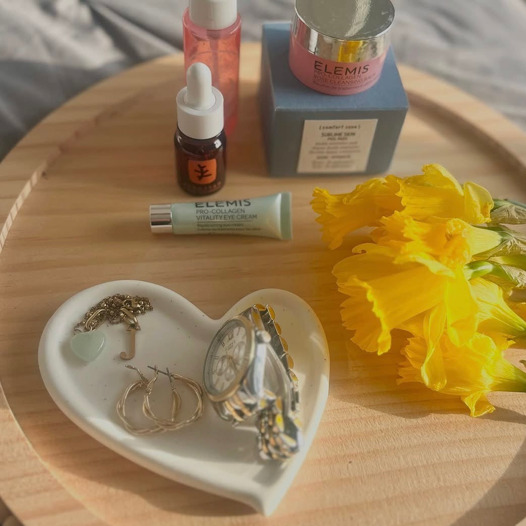 Jewelry set on a heart-shaped tray with skincare products and yellow flowers on a wooden surface