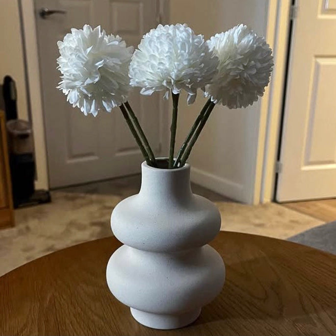 White wavy ceramic vase with artificial hydrangea flowers on a wooden table
