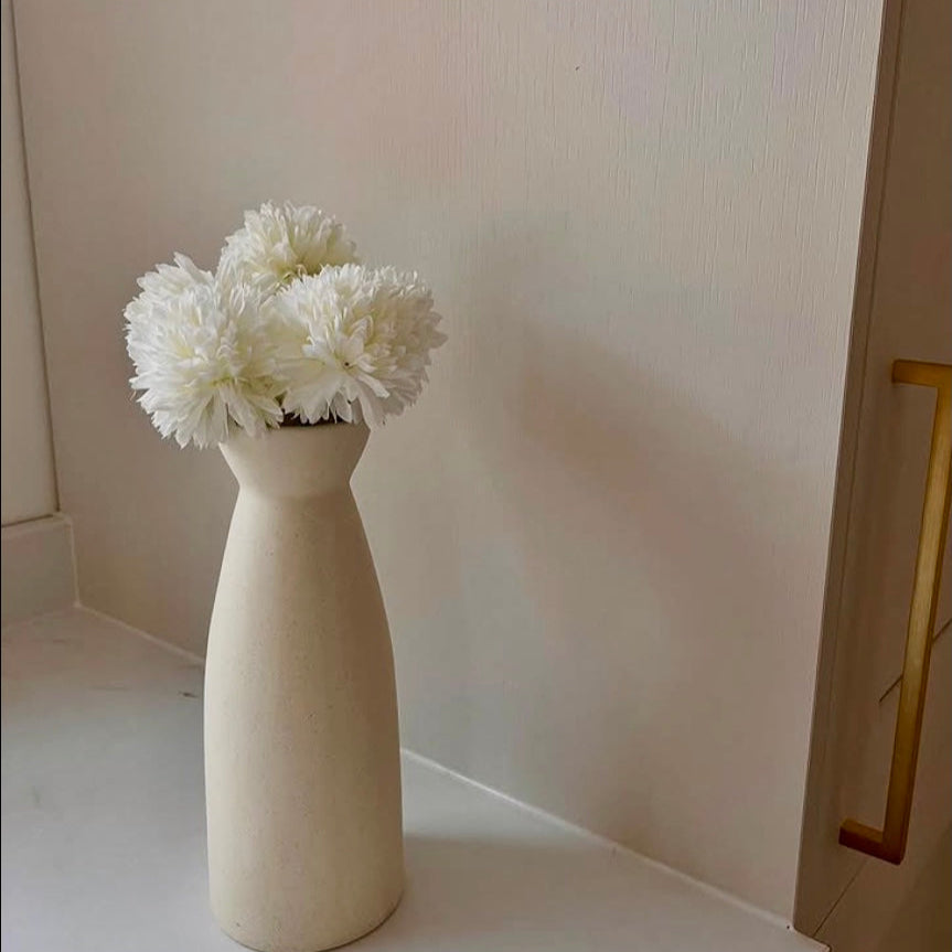 White vase with artificial hydrangea flowers on a light surface against a neutral wall