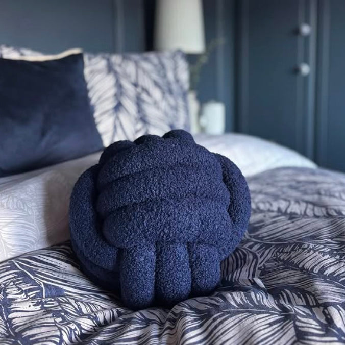 Navy blue knotted pillow on a bed with patterned bedding and pillows.