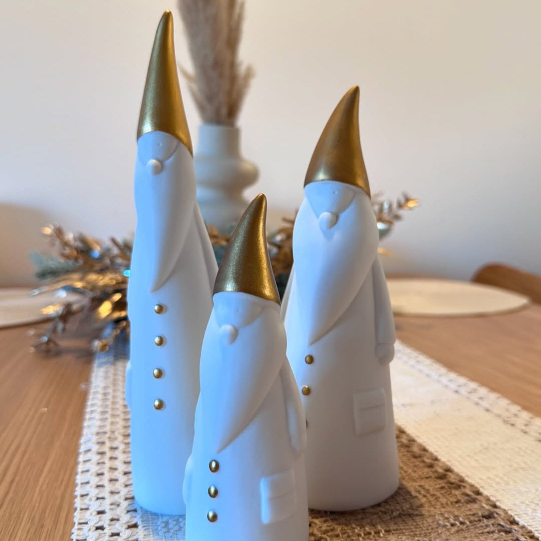 Three decorative figures with gold hats on a table with a lace tablecloth.