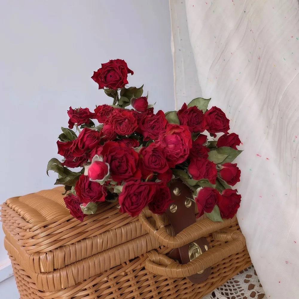 Bouquet of dried red roses on a wicker basket against a white wall.