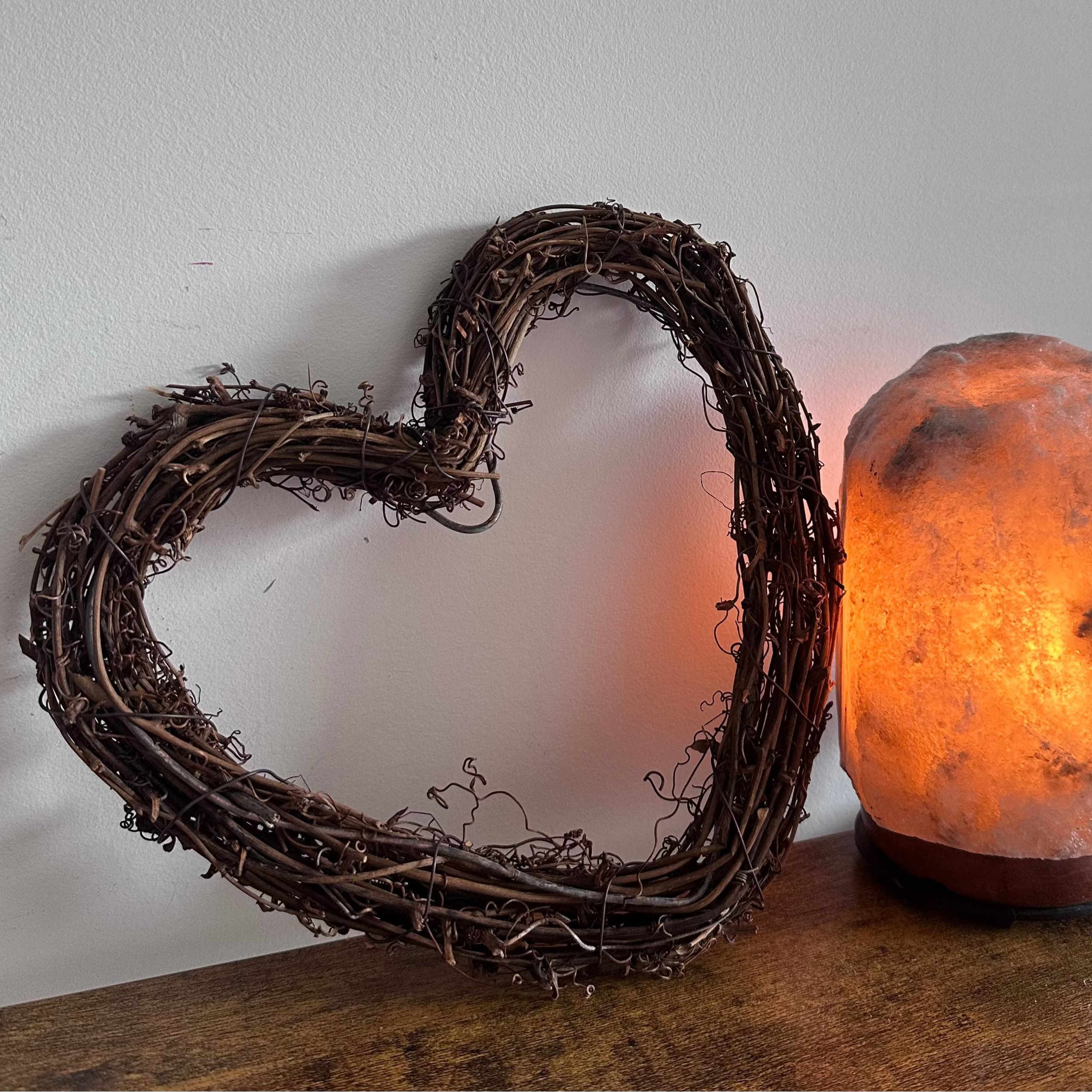Heart-shaped wreath and a salt lamp on a wooden surface with a white wall background