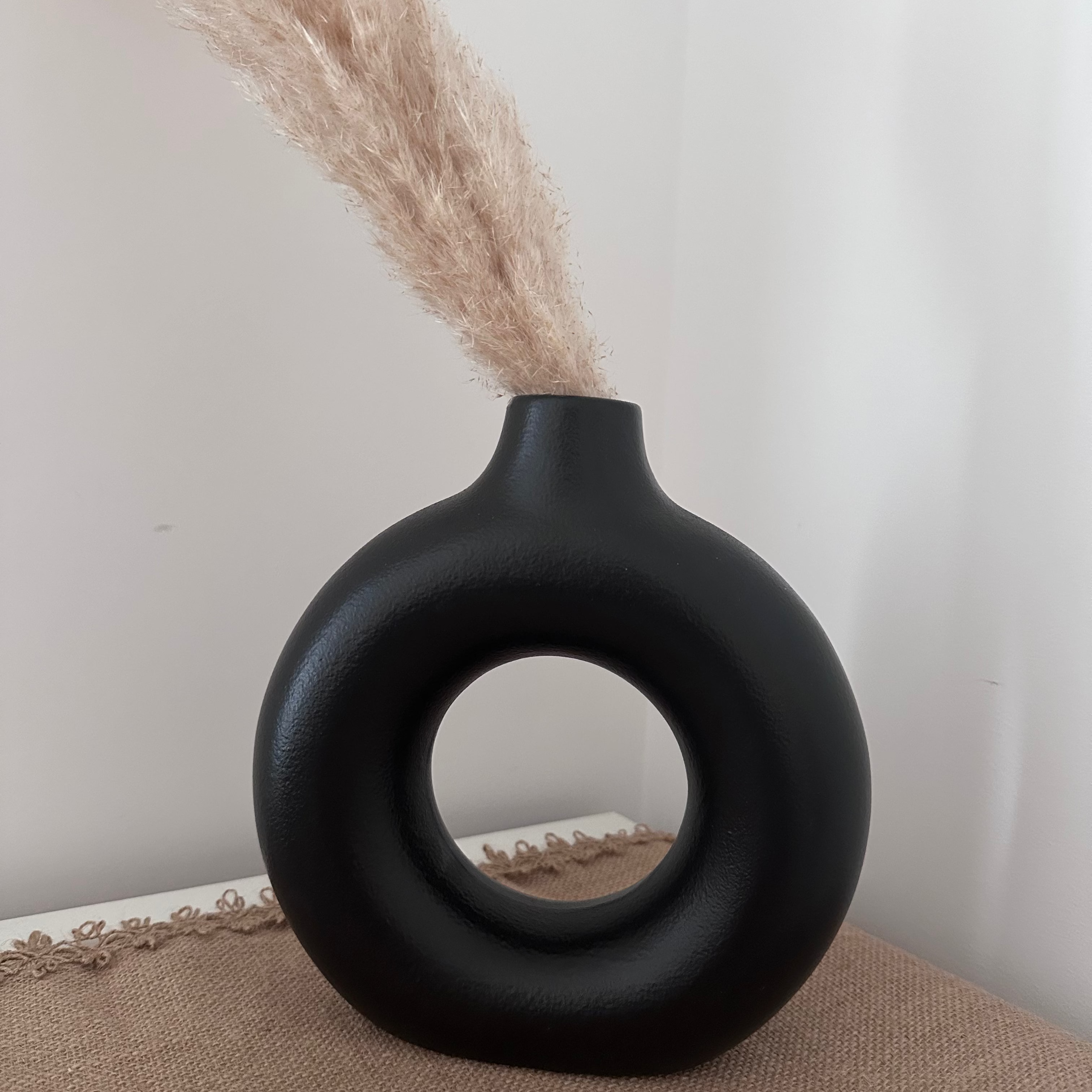 Black nordic vase with circular design on a textured surface with dried plants.
