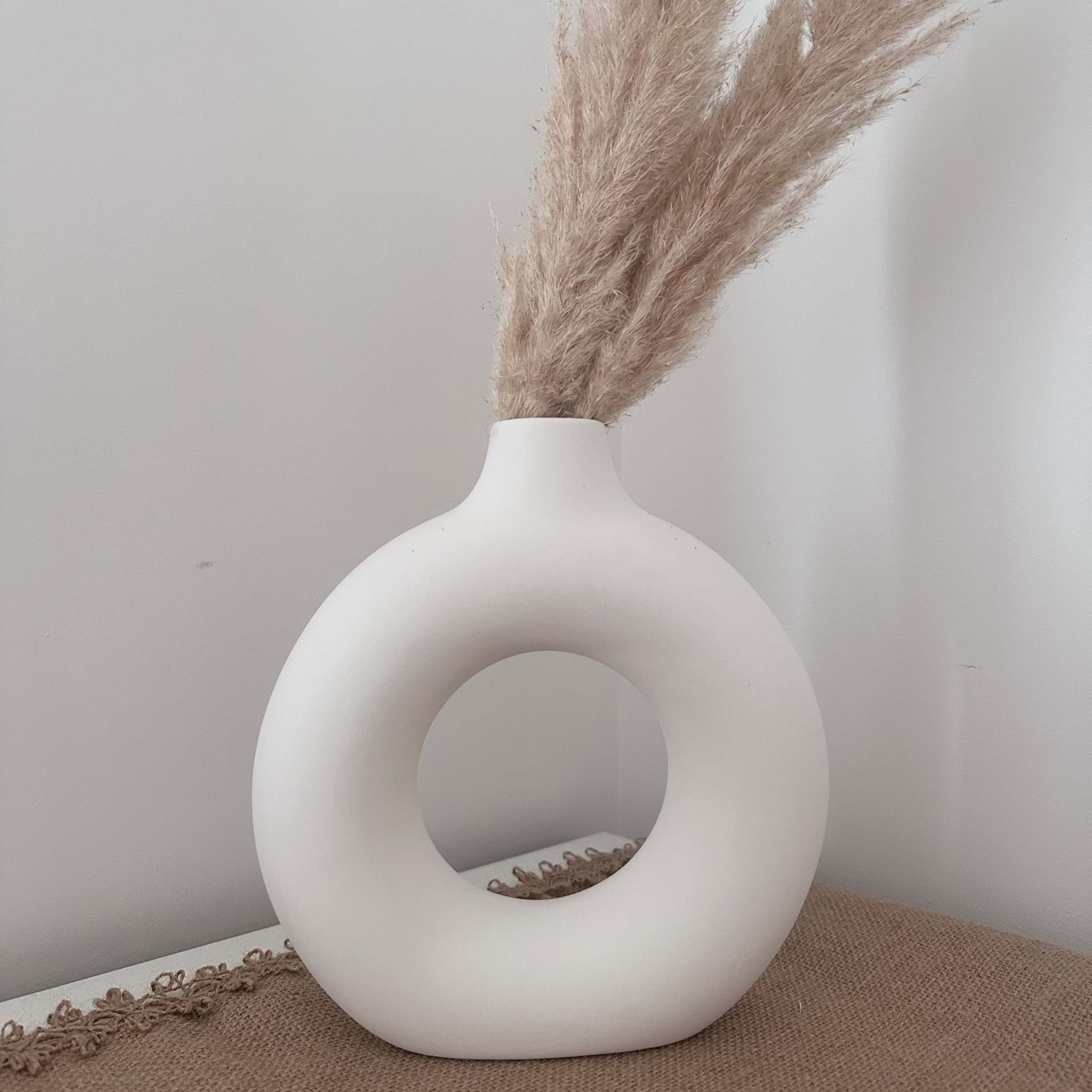 White vase with dried pampas grass against a plain wall