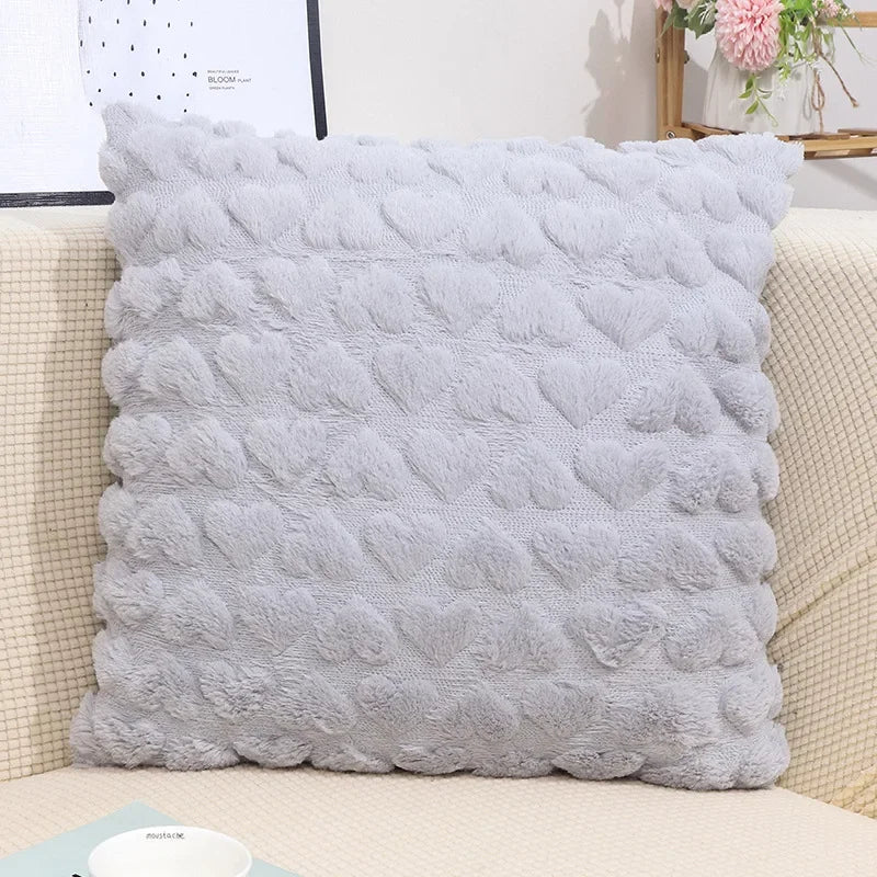 A grey plush love heart pillow cover on a couch, with a textured pattern creating a heart shape.