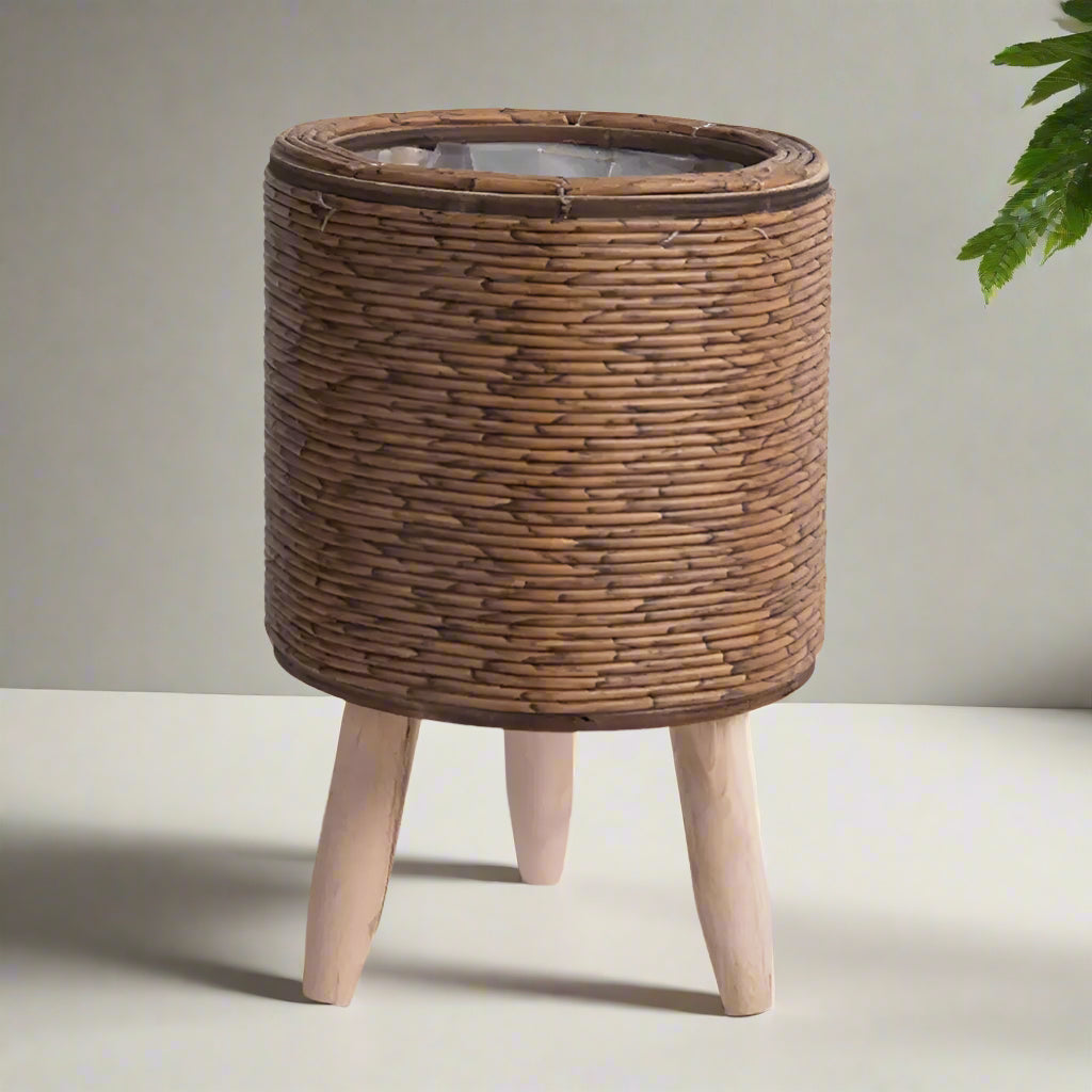 Cylindrical, dark brown wicker flower pot with wooden legs on a light gray background