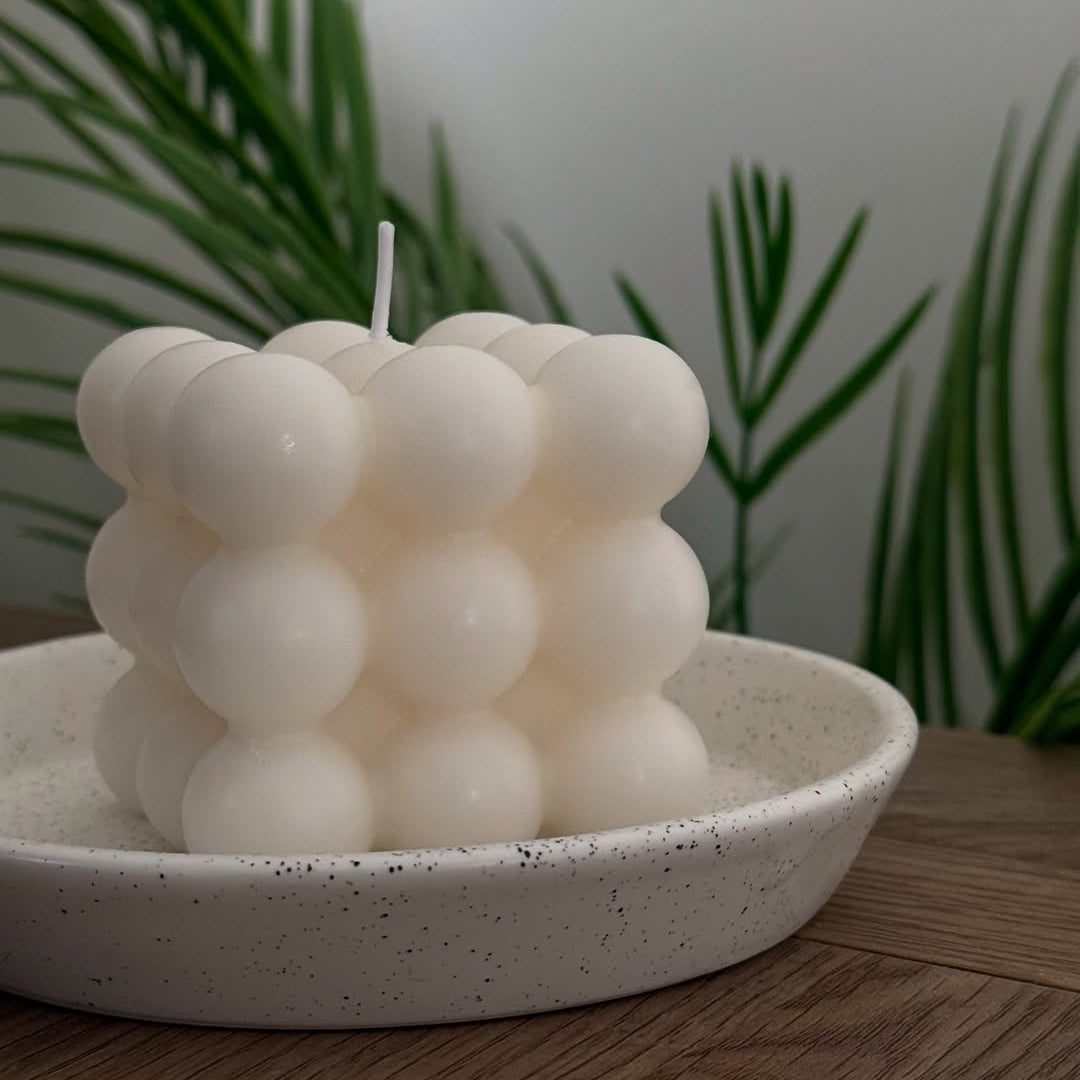 Soy wax candle with a bubble-like design on a speckled ceramic plate with plants in the background