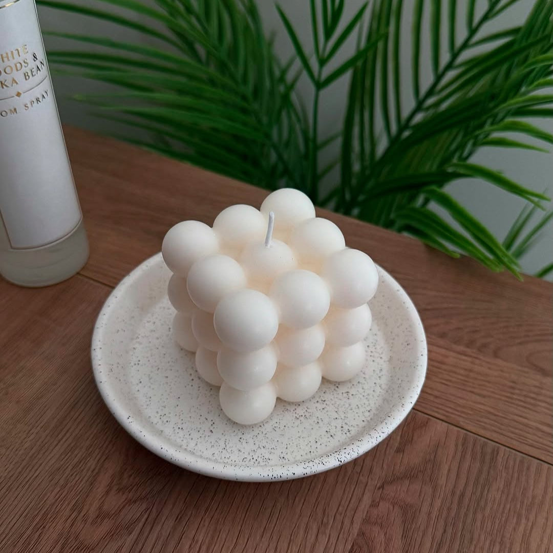 Soy wax candle with a geometric design on a white plate, with a plant and bottle in the background.