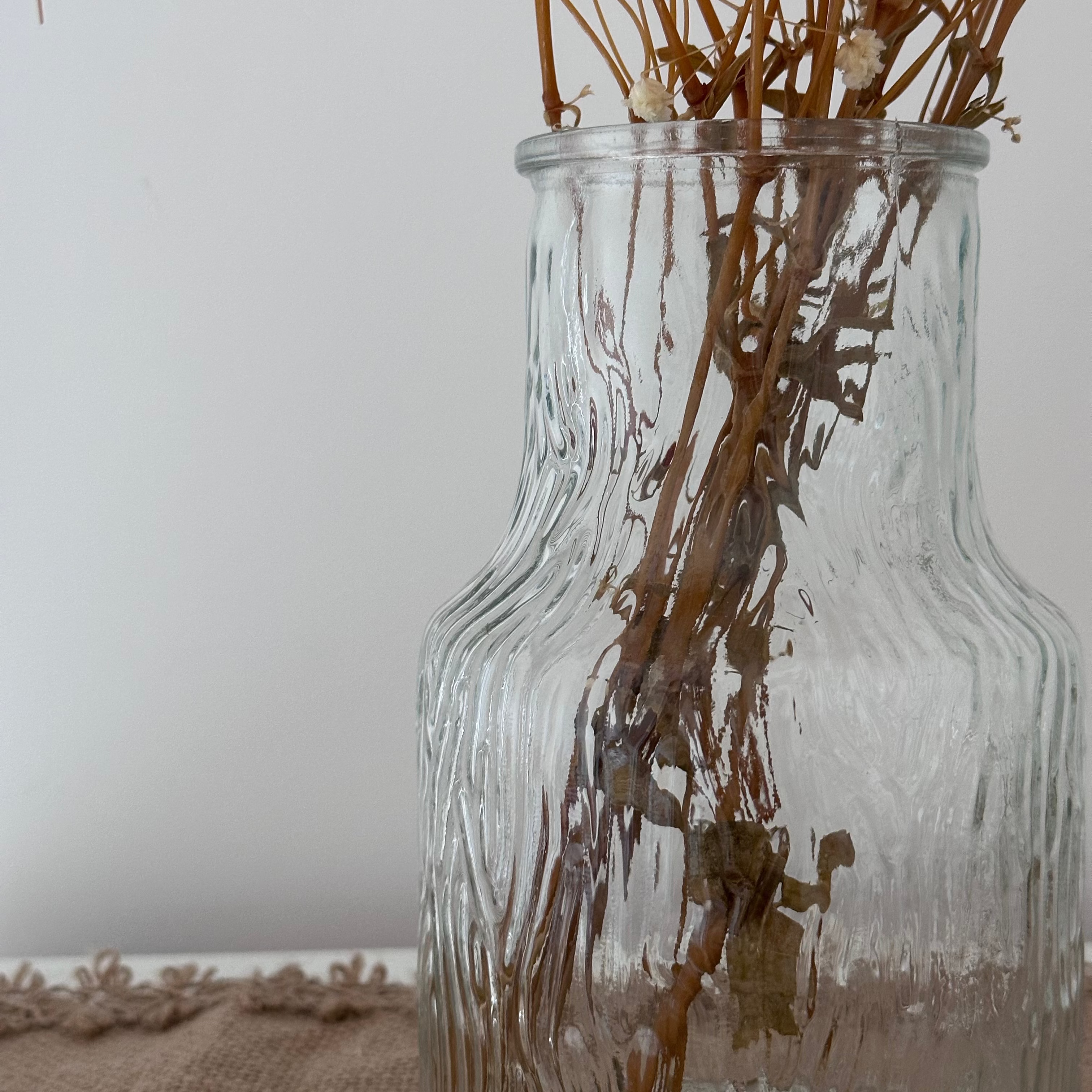 Clear glass vase with dried plants on a neutral background