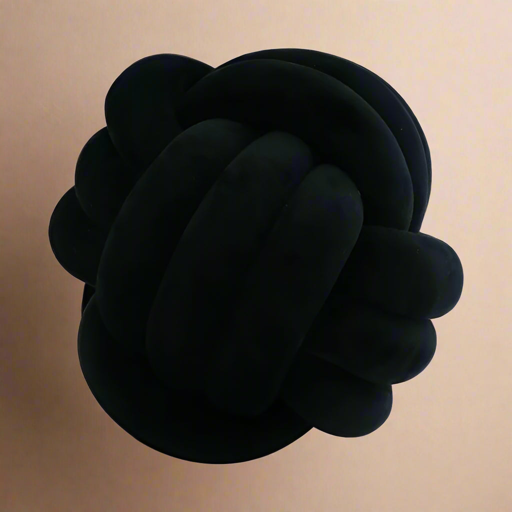 A black knot-shaped cushion against a light beige background.