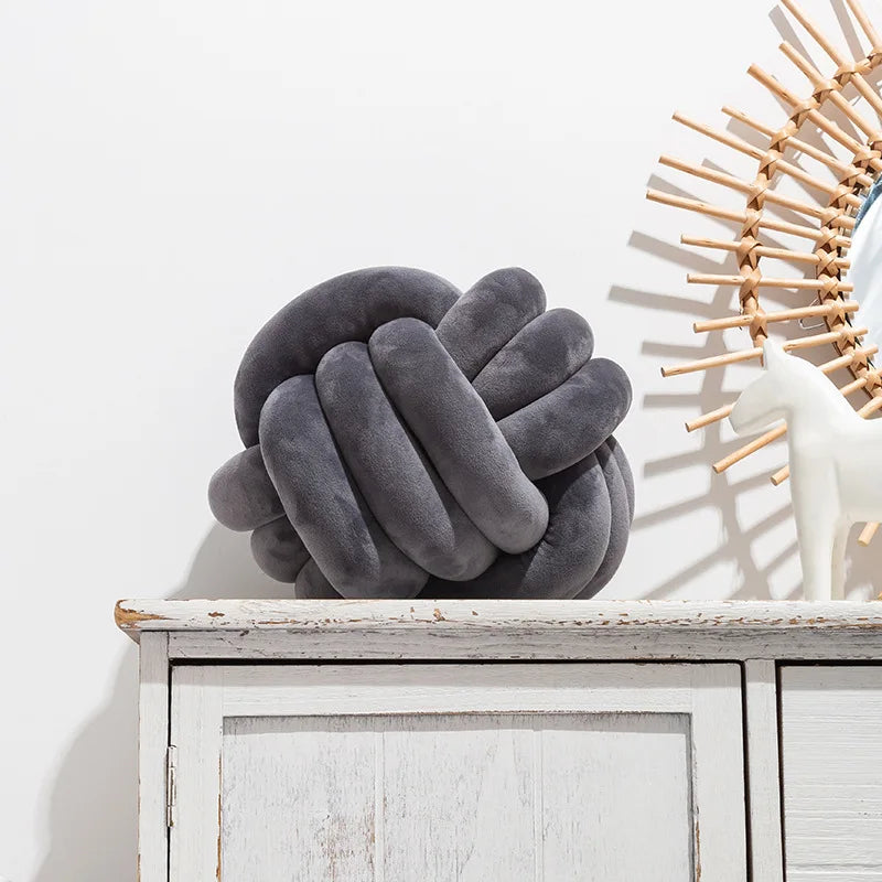 A dark grey knot-shaped cushion styled on a sideboard, next to an ornament.