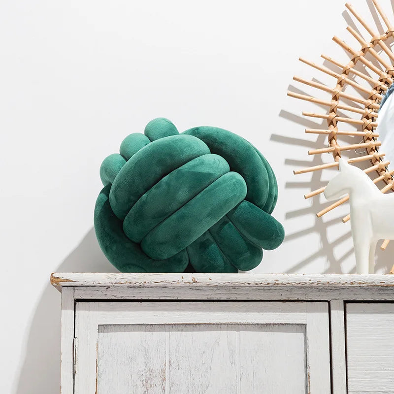 An emerald coloured knot-shaped cushion styled on a sideboard, next to an ornament.