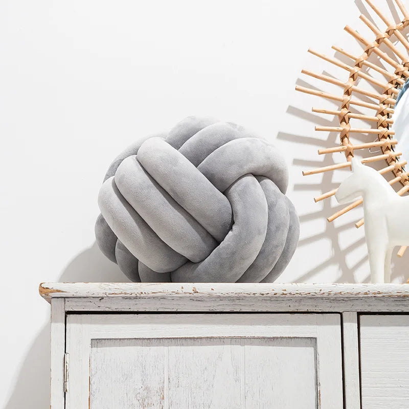 A light grey knot-shaped cushion styled on a sideboard, next to an ornament.