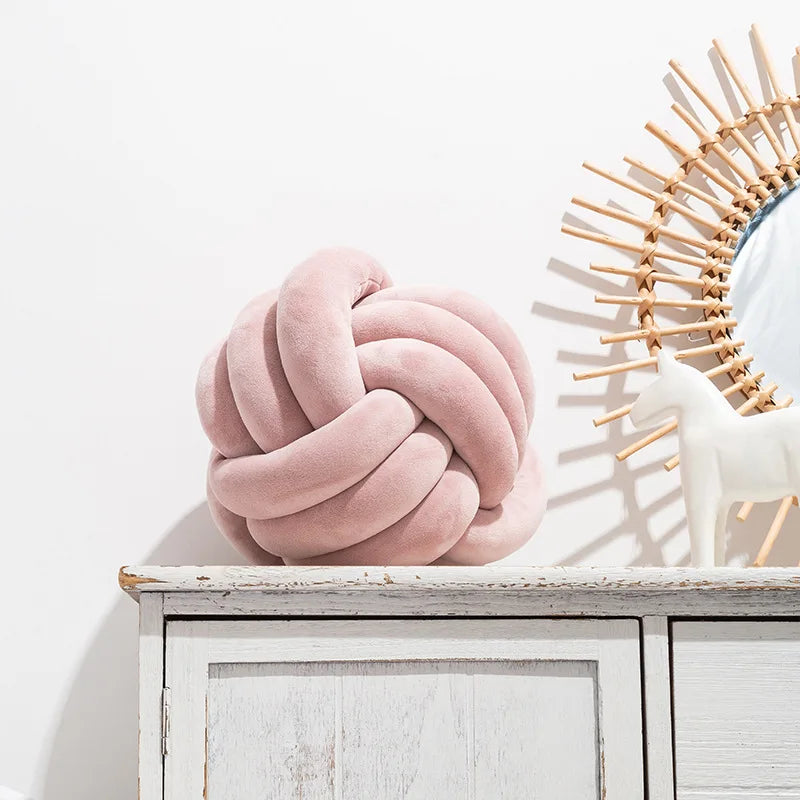 A pink knot-shaped cushion styled on a sideboard, next to an ornament.