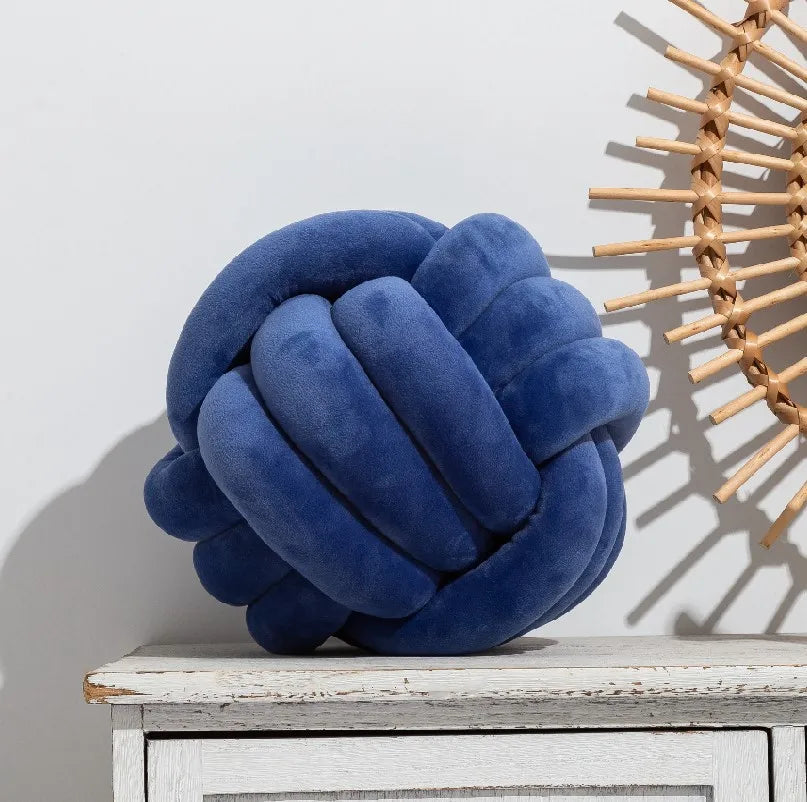 A dark blue knot-shaped cushion styled on a sideboard, next to an ornament.