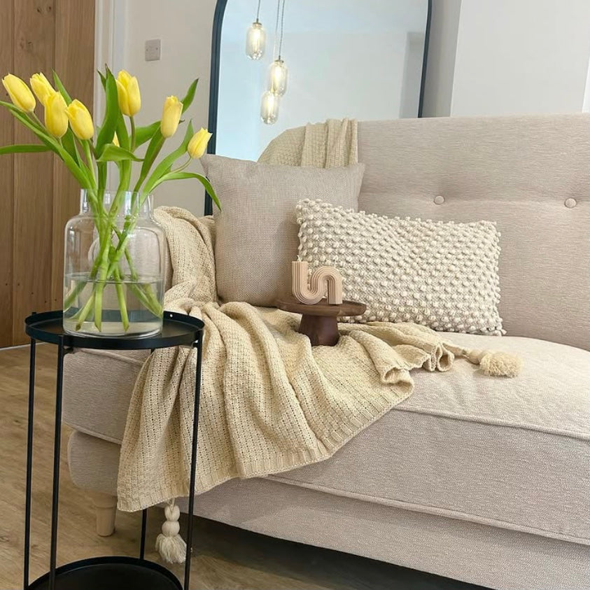 Light grey sofa with decorative pillows, a Nordic waffle blanket and a vase of yellow tulips on a side table.