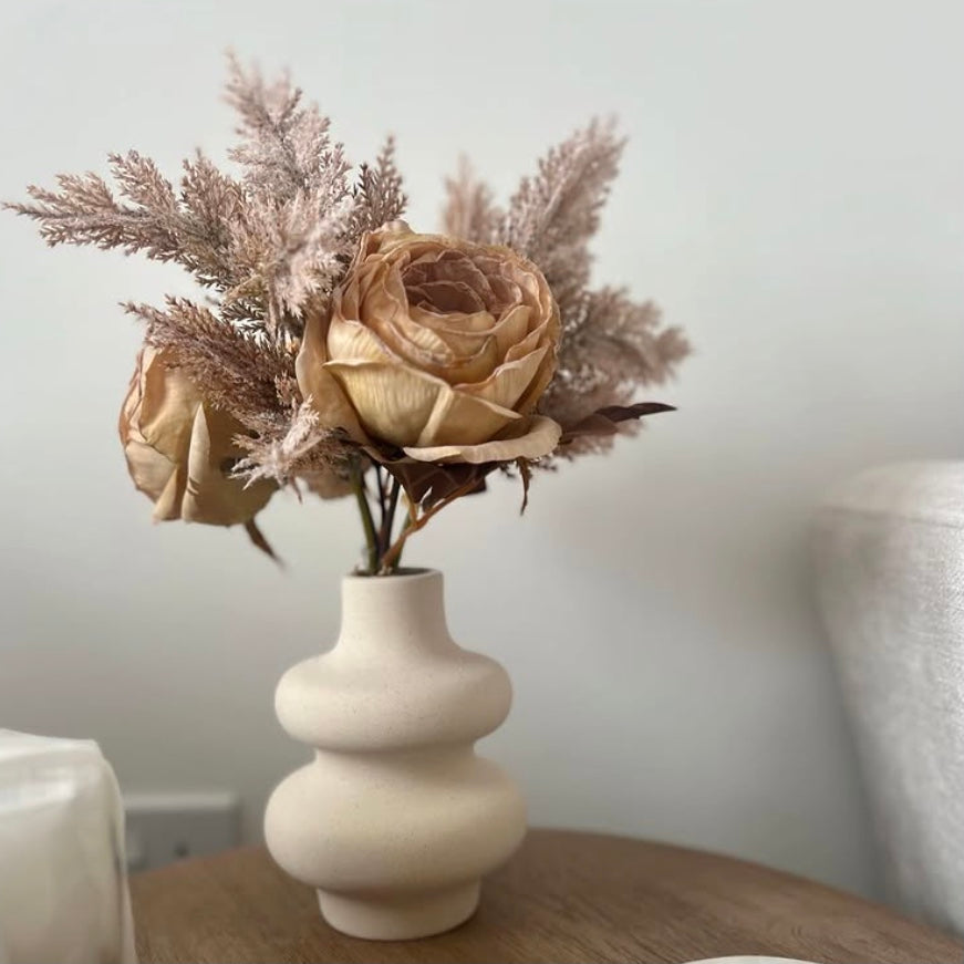 Wavy, white ceramic vase styled with dried flowers in a minimalist setting.