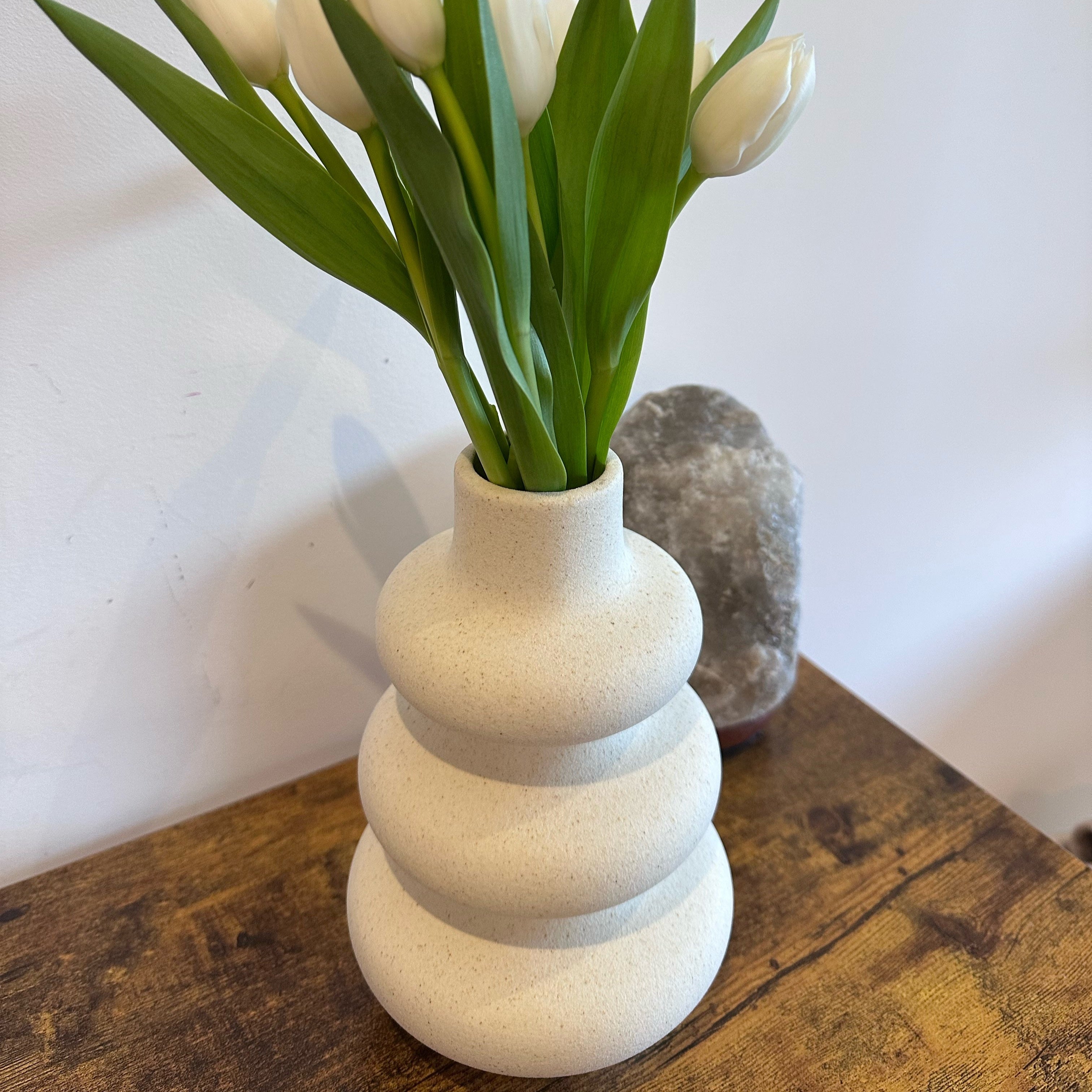 White nordic, wavy vase with tulips on a wooden surface