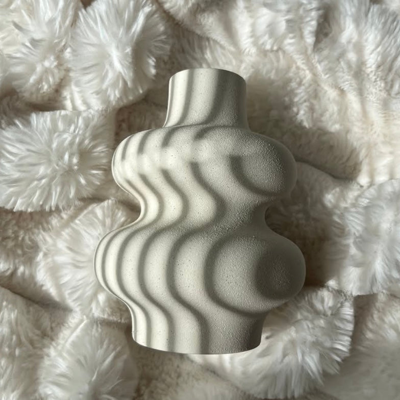 White, wavy ceramic vase styled on a fluffy throw
