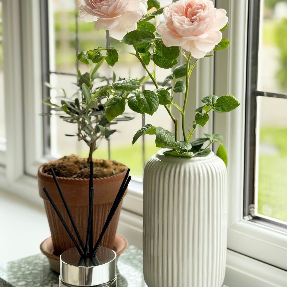 White ceramic, minimalist vase with pink flowers and a potted plant on a windowsill