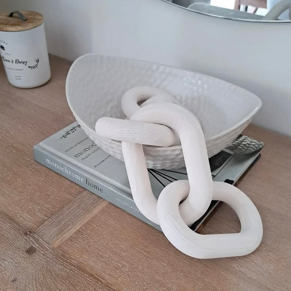 Decorative white knot sculpture on a book with a textured bowl in the background.