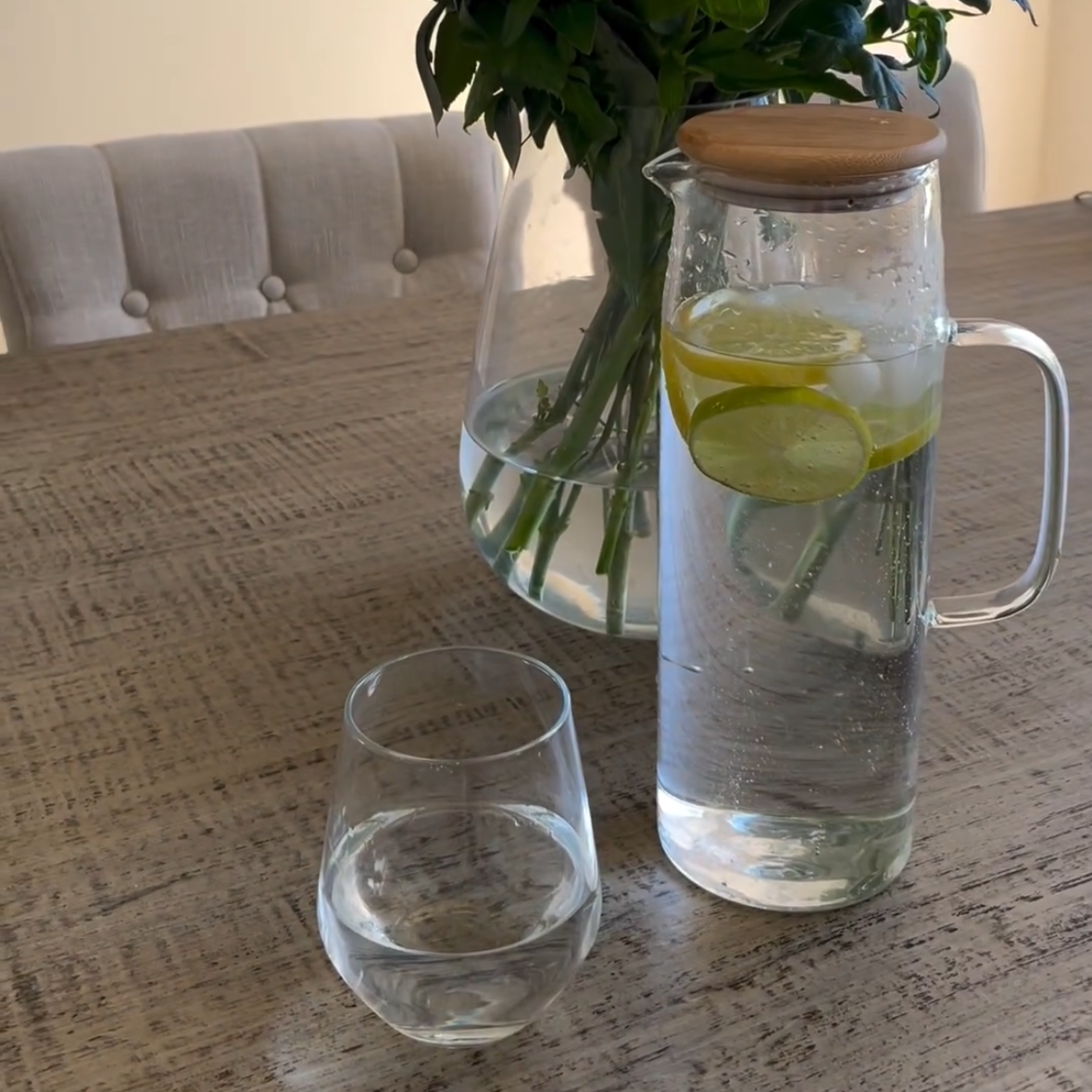 Bouquet of flowers in a vase on a table with a glass and pitcher.