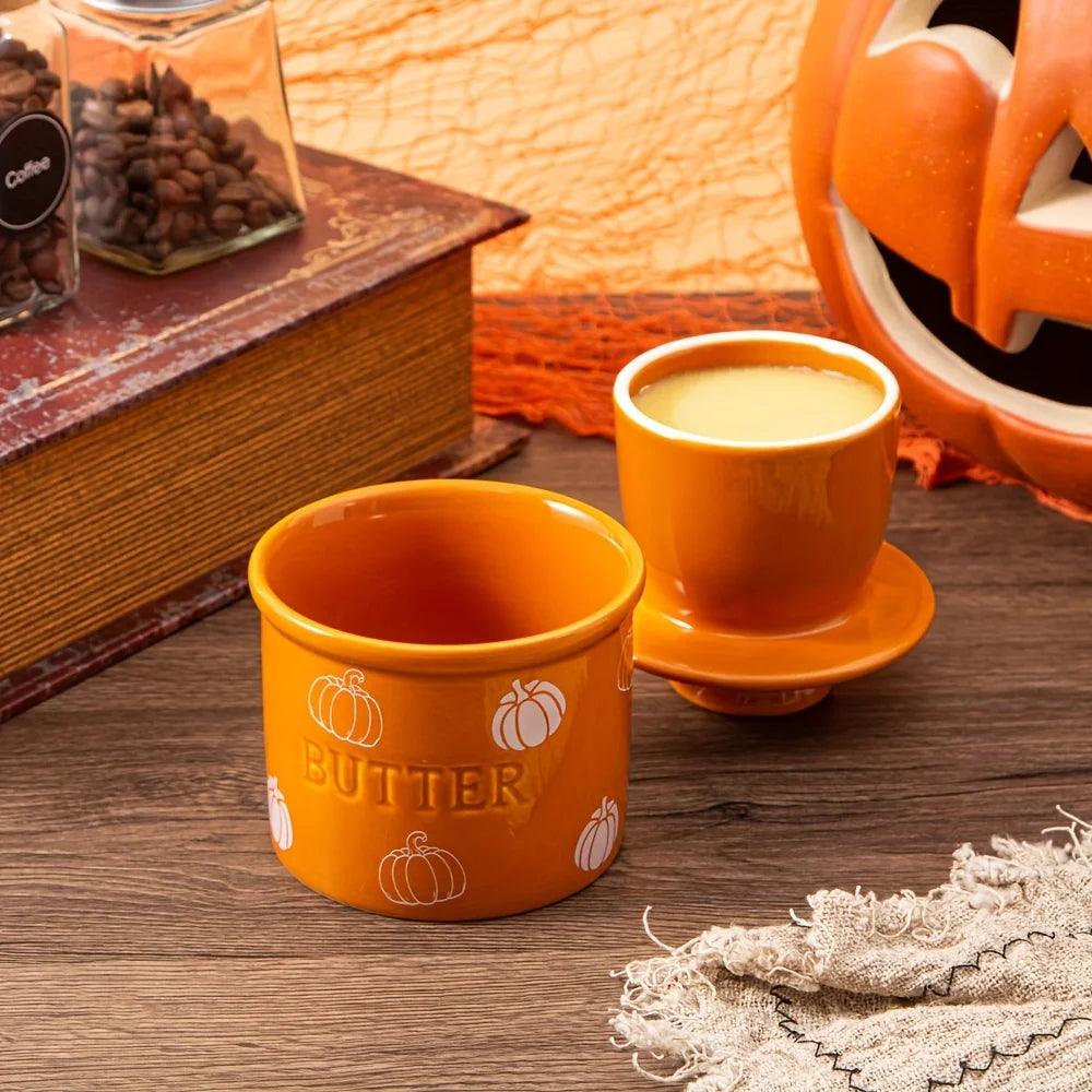 Orange butter container with a pumpkin design on a wooden surface, next to a book and decorative items.