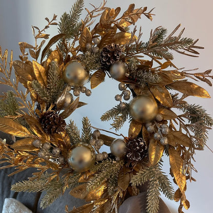 Decorative wreath with gold leaves, pinecones, and silver balls against a neutral background