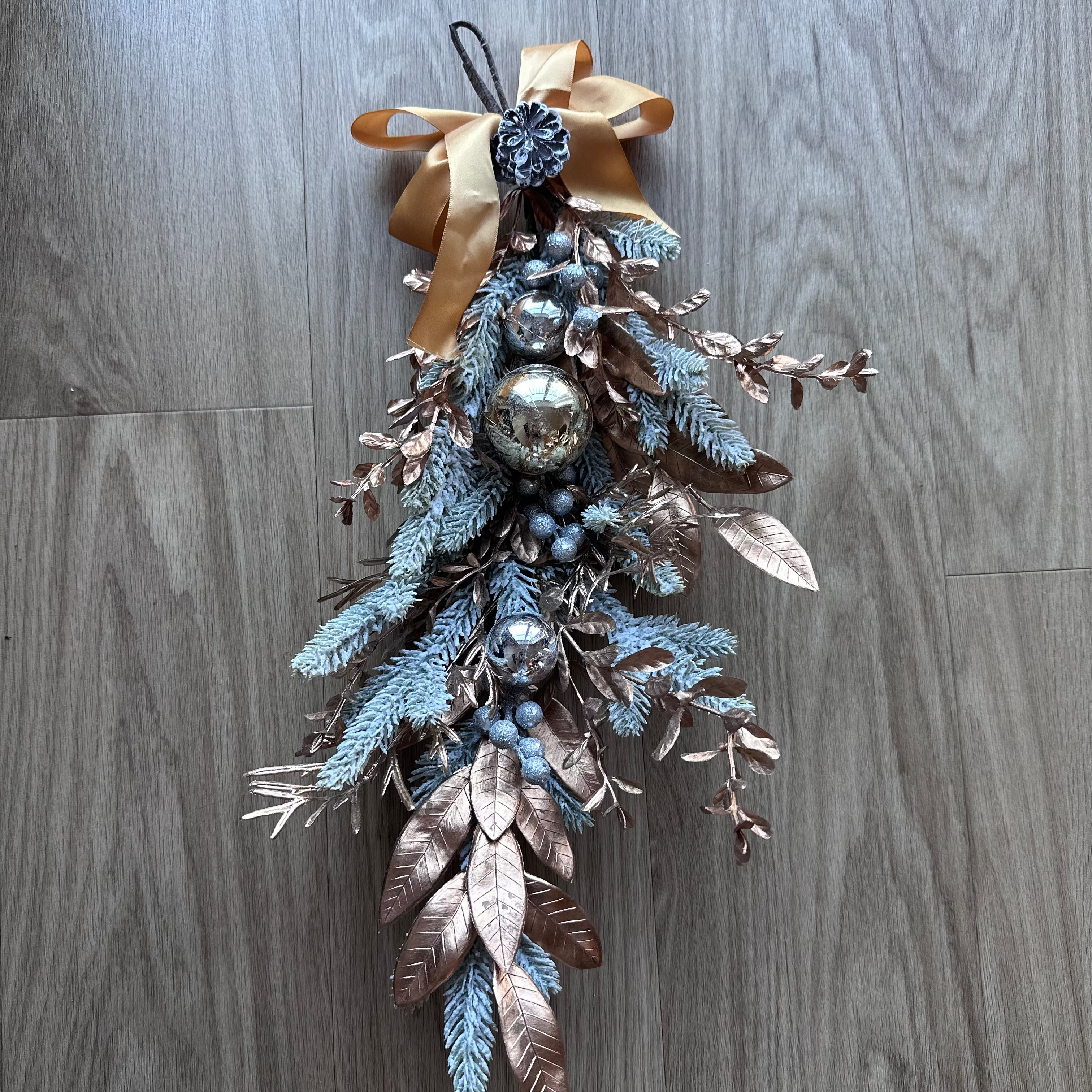 Decorative wall hanging with branches, berries, and a bow on a wooden surface